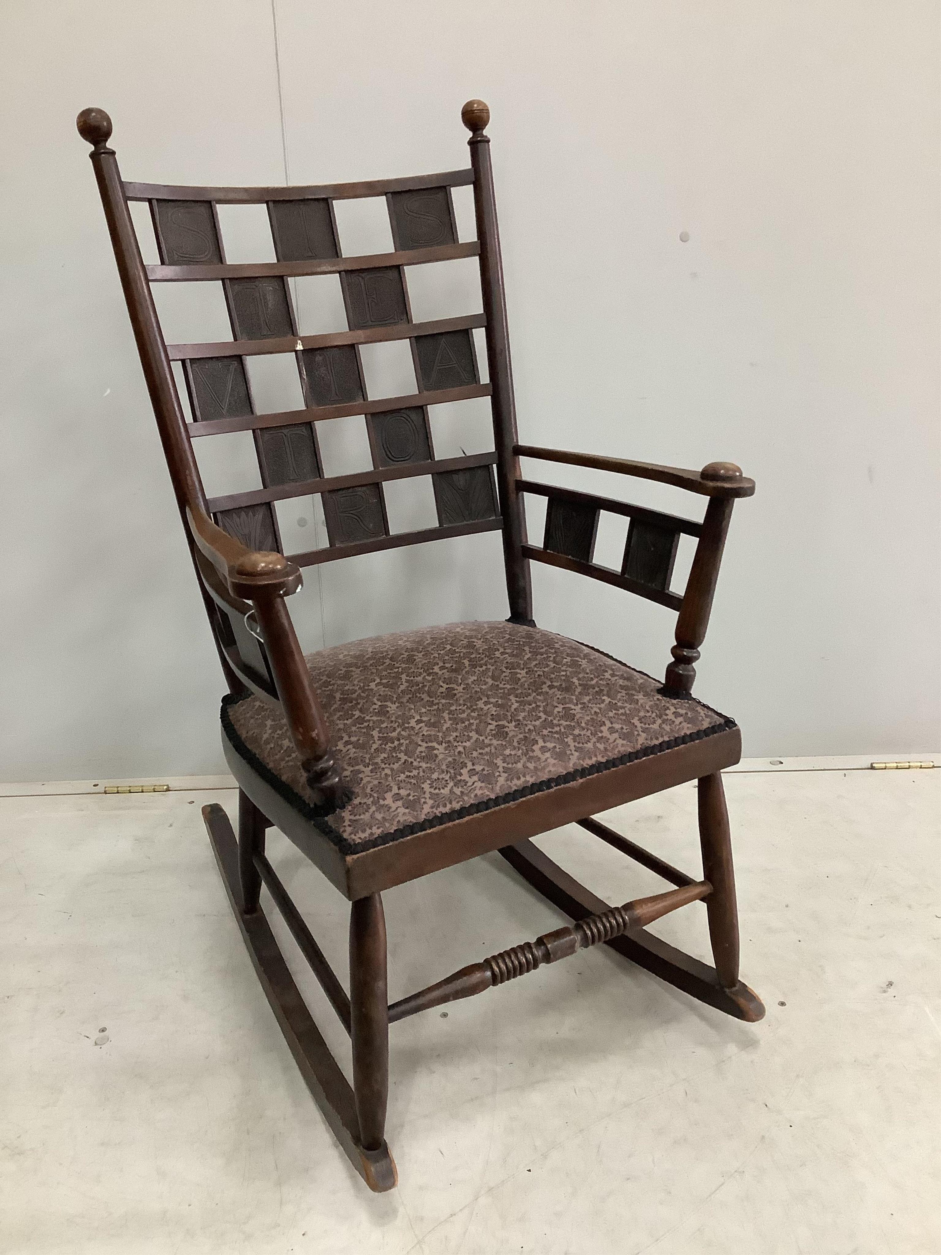 An Arts & Crafts mahogany rocking chair with copper panelled back inscribed 'Siste Viator' (stop, traveler - often used on Roman roadside tombs), width 60cm, depth 45cm, height 108cm. Condition - fair